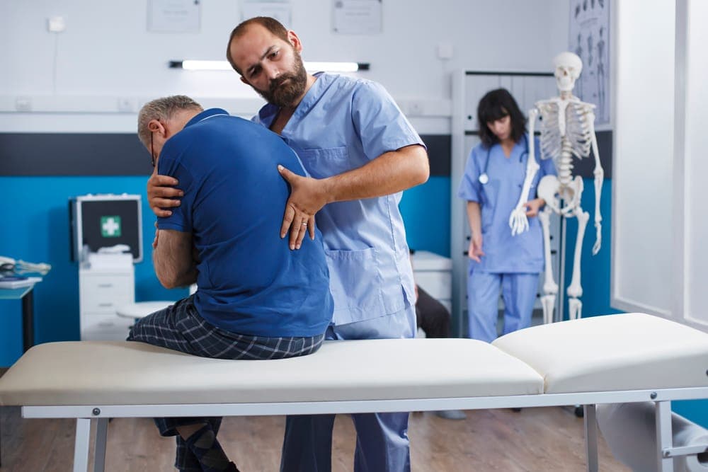 A clinician supporting the lower back of a patient seated on the edge of an exam table