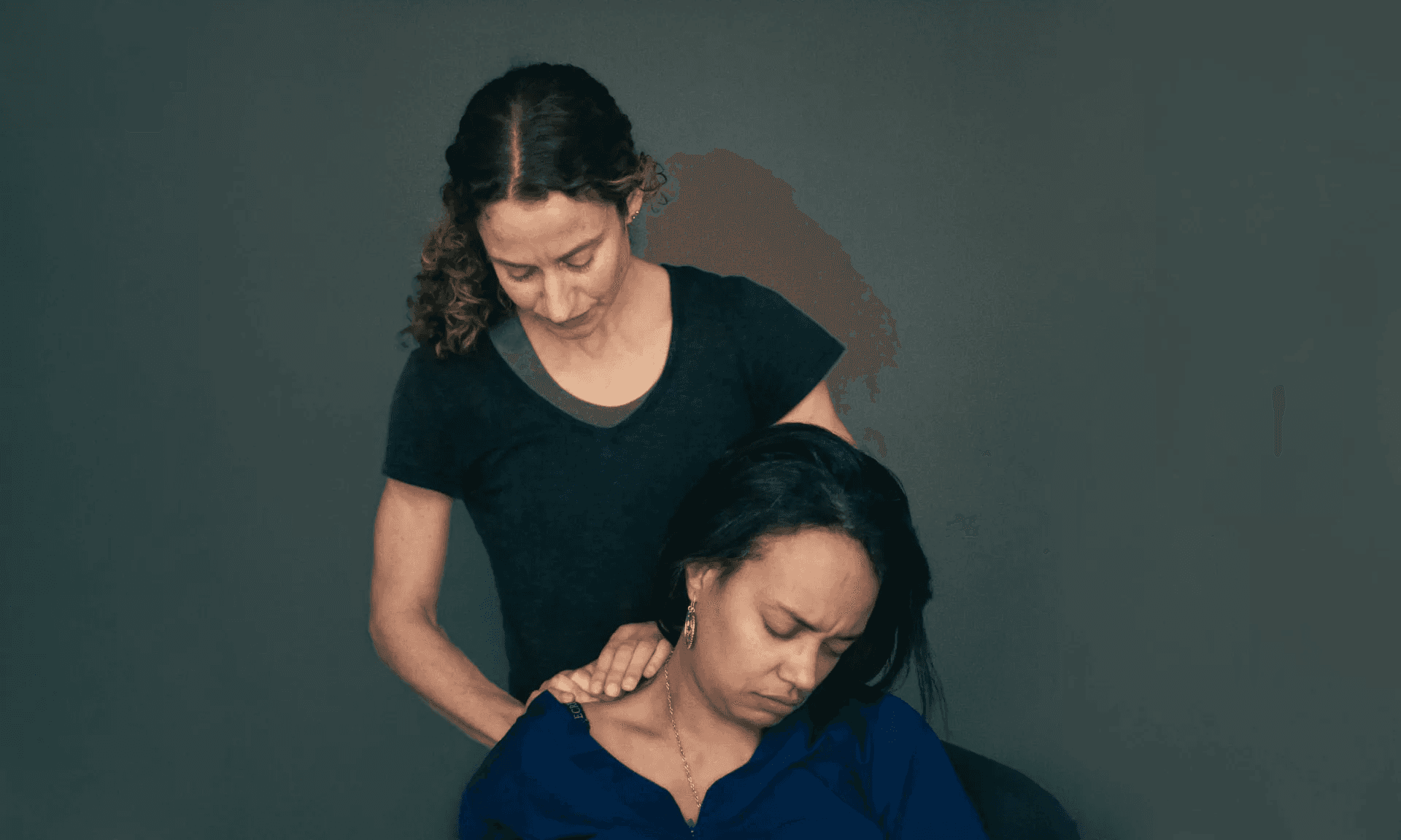 A practitioner standing behind a seated patient, working her fingers into the muscles at the side of the patient's neck
