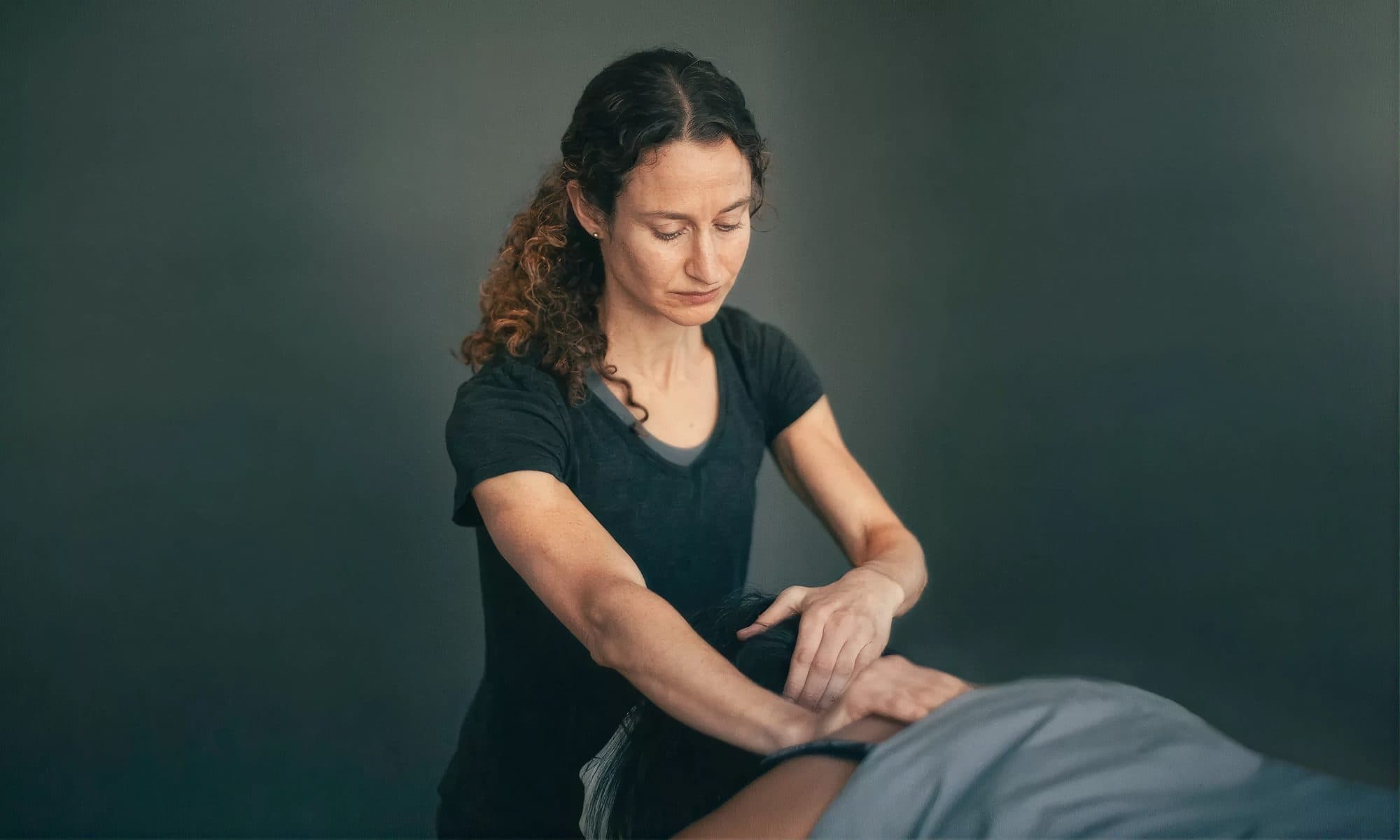 A clinician using both hands to work on the upper back of a patient lying face down on a treatment table