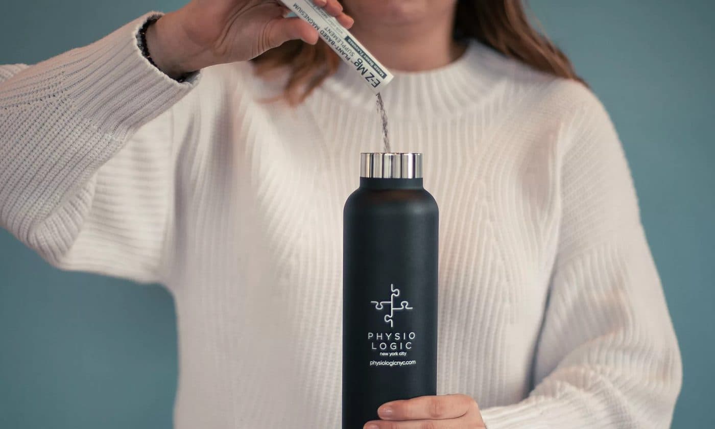 A person in a knit sweater holding a black Physio Logic water bottle and a dropper bottle