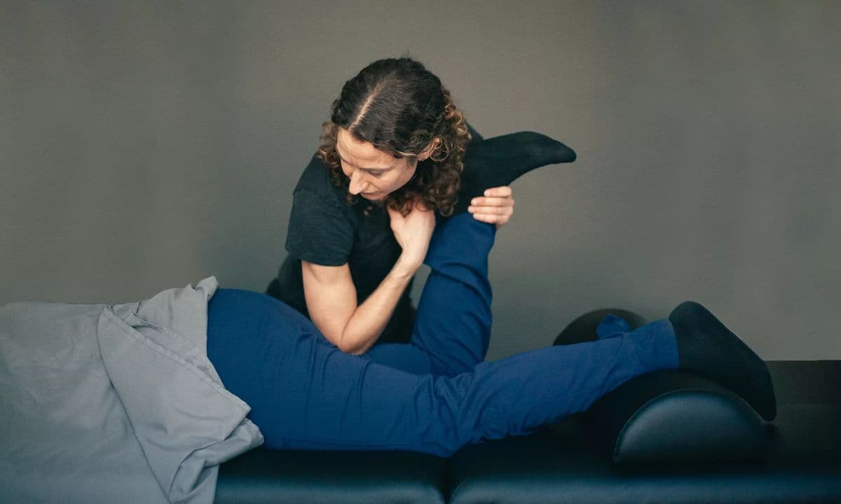 A therapist kneeling beside a side-lying patient and drawing the patient's bent knee toward the chest