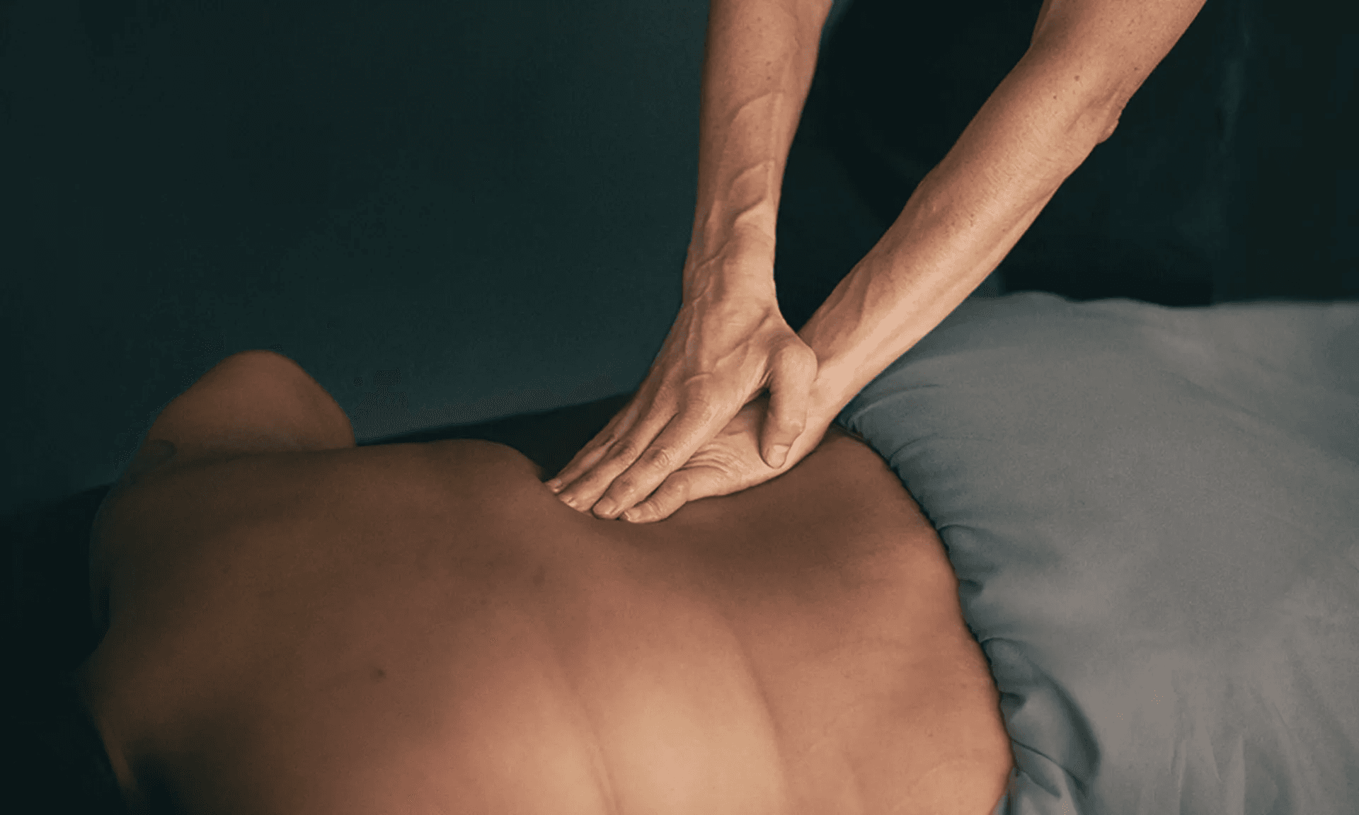 A therapist pressing with both hands along the mid-back of a patient lying face down under a sheet
