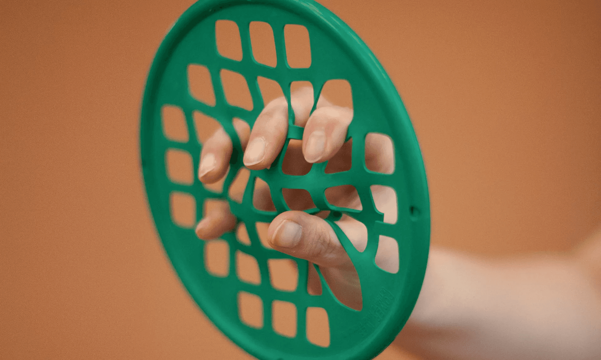 A patient's fingers stretching apart the squares of a green hand-exerciser web