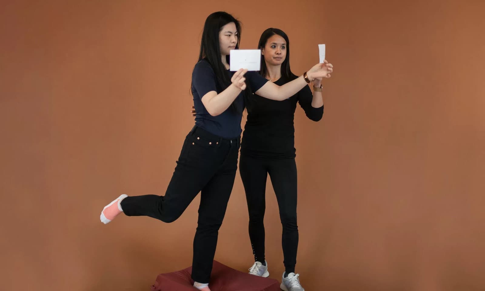 A therapist steadying a patient balancing on one leg while she tracks a card held at eye level