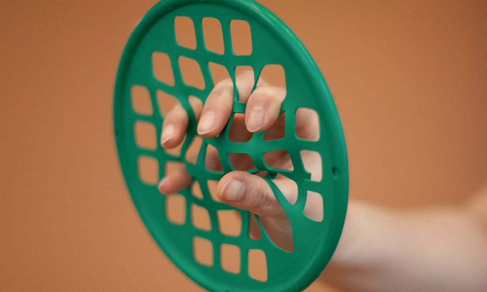 A patient stretching their fingers inside a green resistance web hand exerciser