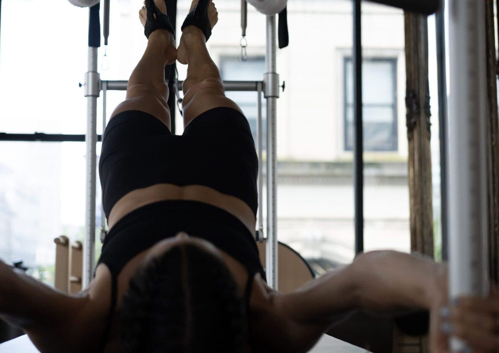 A client lying back on a Pilates trapeze table with both feet strapped into the tower, seen from above