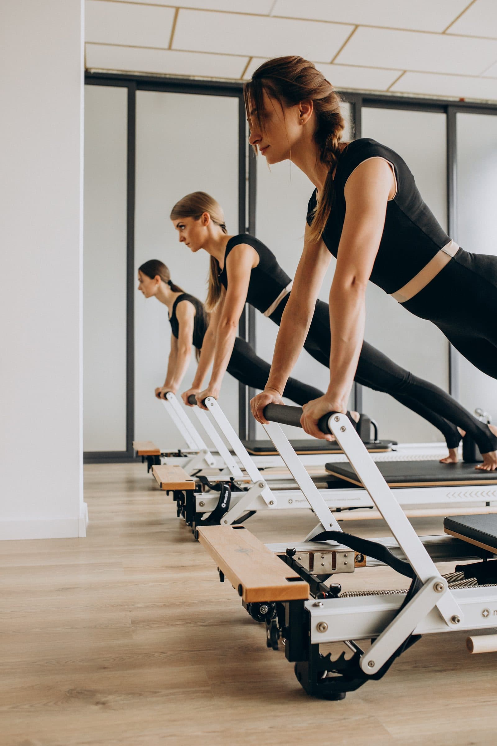 Three people in black activewear holding a plank position on Pilates reformers in a bright studio