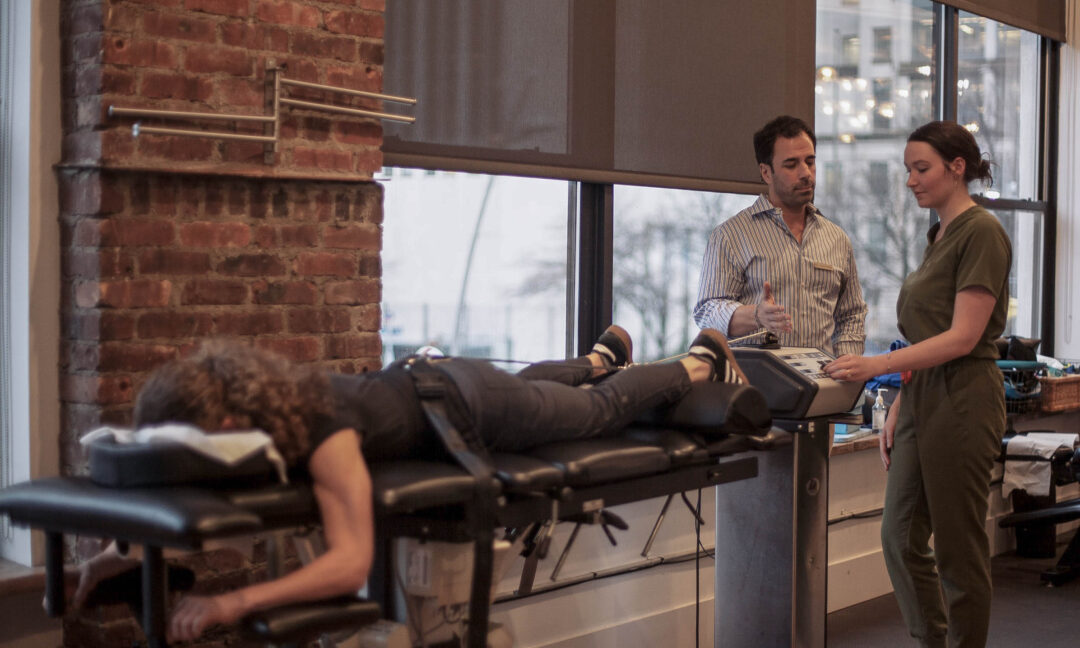 Chiropractor explaining spinal decompression machine to patient during chiropractic care session in Brooklyn clinic.